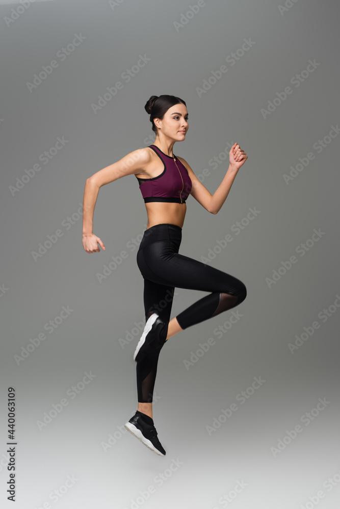 full length view of sportive woman jumping on grey background.