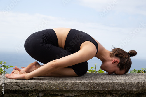 Woman doing yoga on the top of a mountain on a sunny day.Girl on a mountain striking a balance yoga pose feeling at peace with nature.Young woman doing yoga outdoors with amazing back view. Bali.