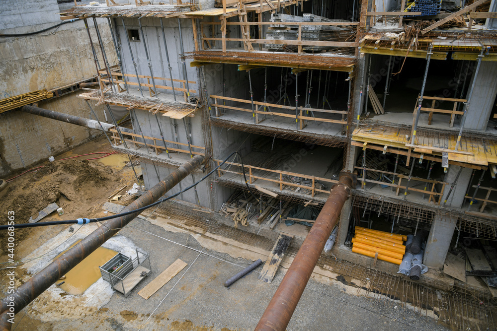 Reinforced concrete basement of high-rise residental building under construction in new city district. Concrete pouring, metal frame piles, steel rods, tower cranes.