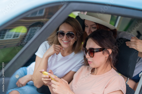 Three happy girlfriends go on a trip. Women are driving in a car and taking a selfie on a mobile phone © Михаил Решетников
