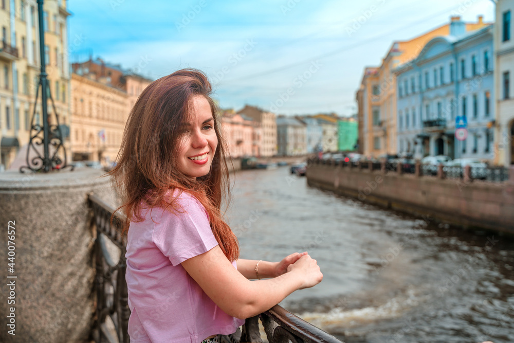 A beautiful young woman walks through the city center along the canals on a summer day, a popular tourist destination of St. Petersburg