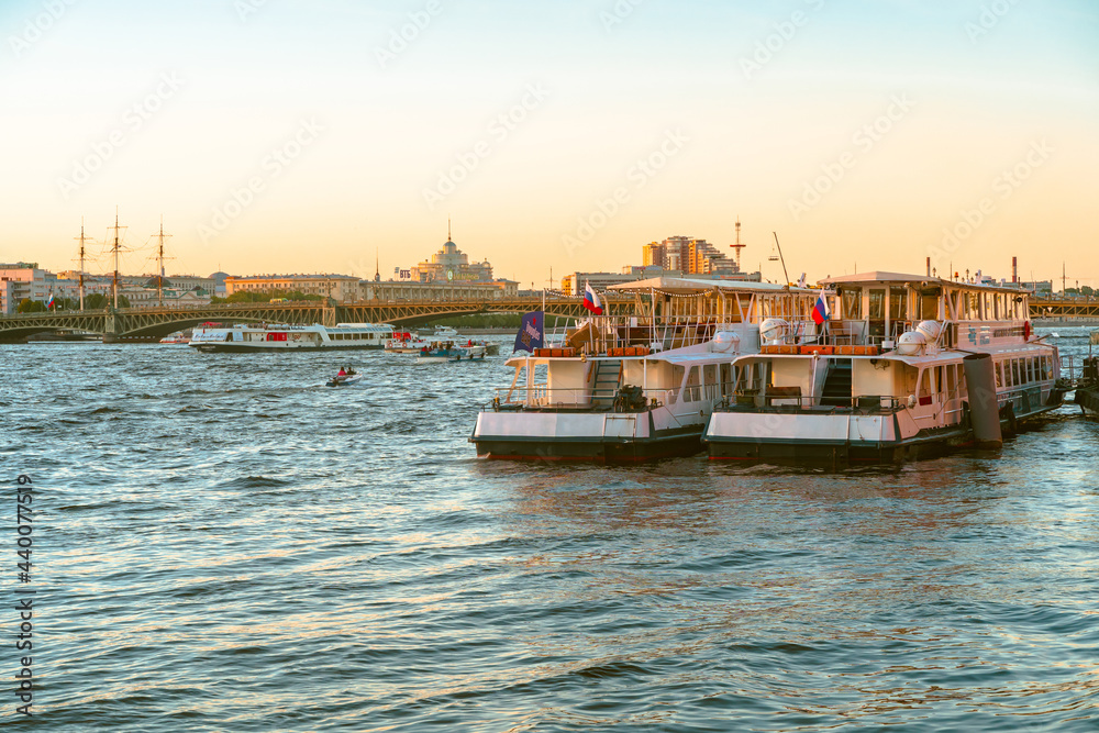 Fototapeta premium Panoramic view of the beautiful sunset over the Neva River in St. Petersburg and pleasure boats with tourists. Saint Petersburg, Russia - 05 Apr 2021