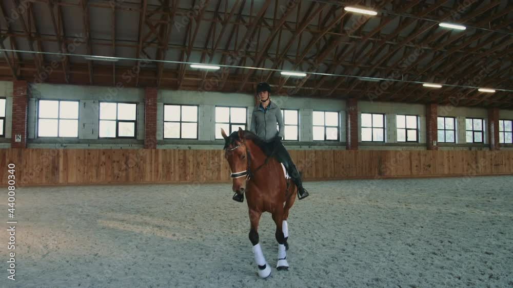 Woman on horse walking slowly on arena. Young woman sitting on horseback and riding on covered sandy arena having practice. Woman on horse walking slowly on arena. Young woman sitting on horseback and riding on covered sandy arena having practice.