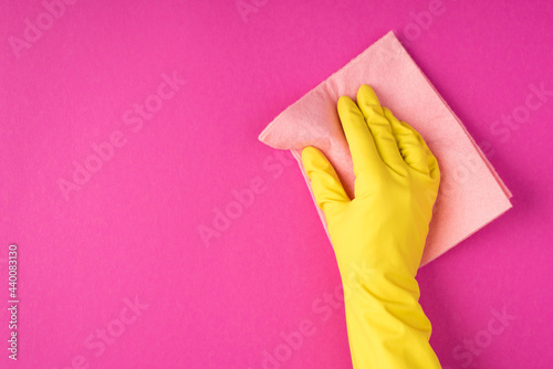 Top view photo of hand in yellow glove using pastel pink viscose rag on isolated pink background with blank space