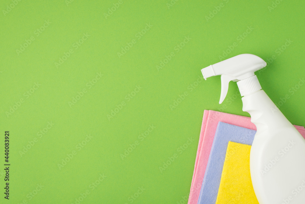 Top view photo of white spray detergent bottle without label on multicolor viscose napkins on isolated green background with blank space Top view photo of white spray detergent bottle without label on multicolor viscose napkins on isolated green background with blank space