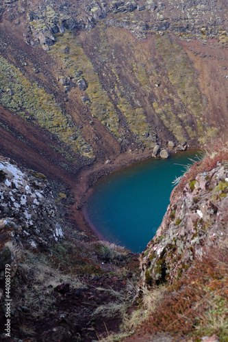 Clear deep blue lake  that mirrors the surrounding water table at the bottom of Icelands Kerid Crater surrounded by red volcanic rock