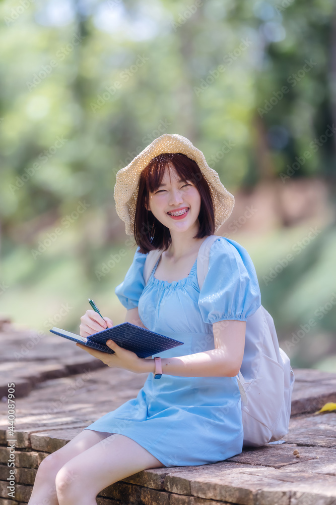 Obraz premium Asian woman tourism and notebook in hand sit on old brick wall at Wat Pha Sak, Chiang san, Chiang rai, Thailand.