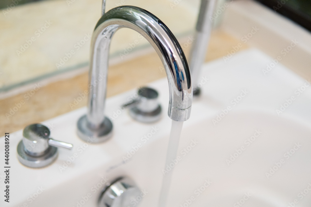 Clear water is running from shiny faucel into the sink in bathroom, closeup view. Water system in residental real estate concept. Clear water is running from shiny faucel into the sink in bathroom, closeup view. Water system in residental real estate concept.