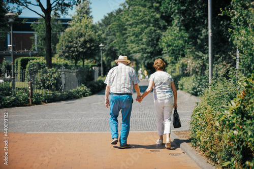 old couple walking hand in hand on street in front of trees