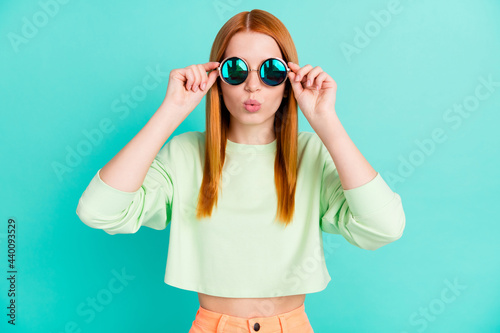 Photo of shiny impressed young woman wear green shirt arms dark glasses lips pouted isolated teal color background