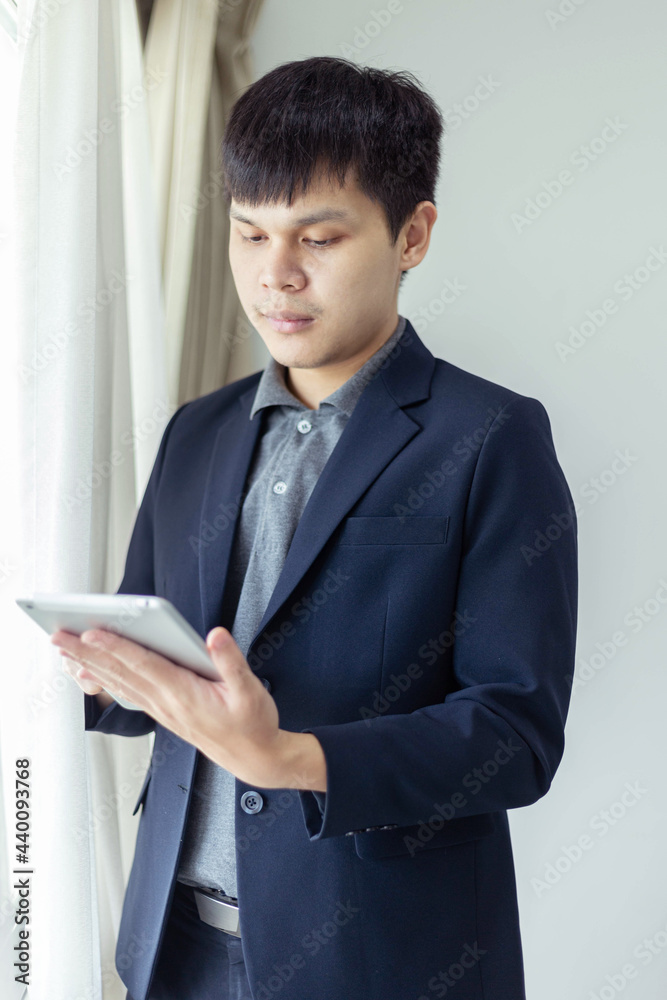 Business partners concept a young businessman wearing navy suit jacket looking on the tablet screen checking an email inbox Business partners concept a young businessman wearing navy suit jacket looking on the tablet screen checking an email inbox