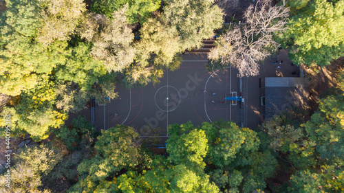 Kids playing basketball in the park, 4K aerial top-down view of a basketball court surrounded by the green trees.