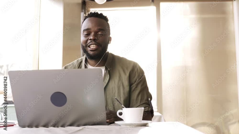 Young african man doing a video call using computer laptop at pub bar restaurant