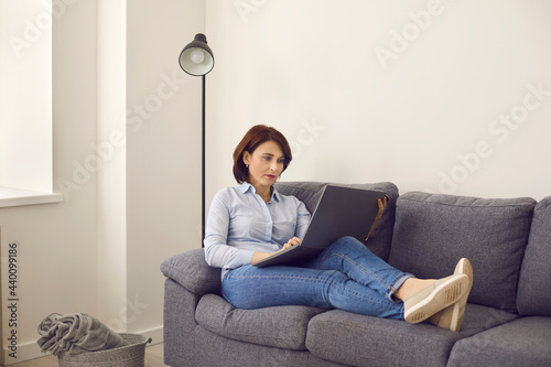 Middle age caucasian woman typing, shopping , browsing or chatting online on laptop keyboard sitting on sofa. Freelance work on computer project, order goods on internet, communication concept