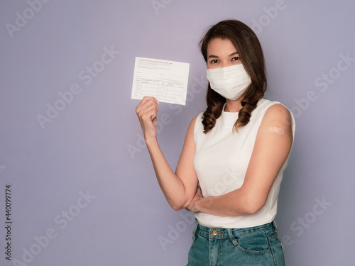 Woman wearing medical protective hygiene mask with band-aid plaster on arm holds and showing vaccinated record card after receives vaccine for coronavirus vaccination campaign concept photo