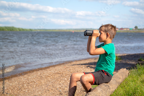 a boy on the river bank looking through binoculars