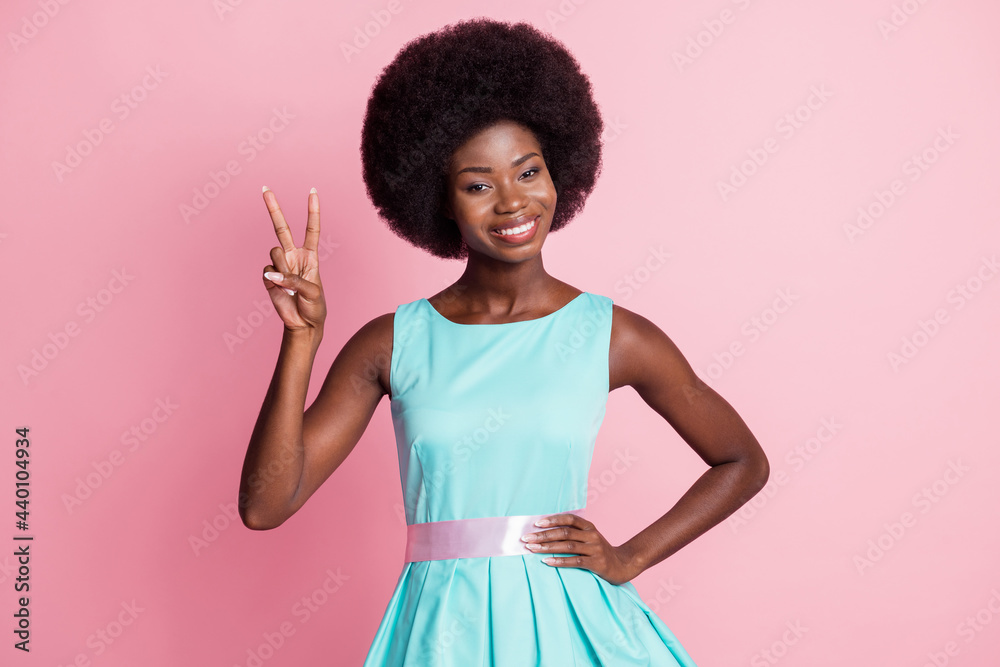 Photo portrait of pretty girl showing v-sign gesture two fingers smiling in blue dress isolated on pastel pink color background Photo portrait of pretty girl showing v-sign gesture two fingers smiling in blue dress isolated on pastel pink color background