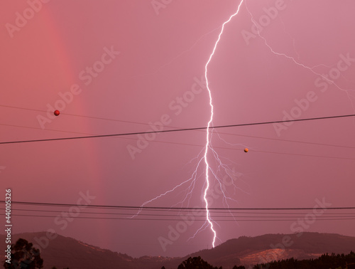 Lightning strike, rainbow and red tones skies in a stormy afternoon