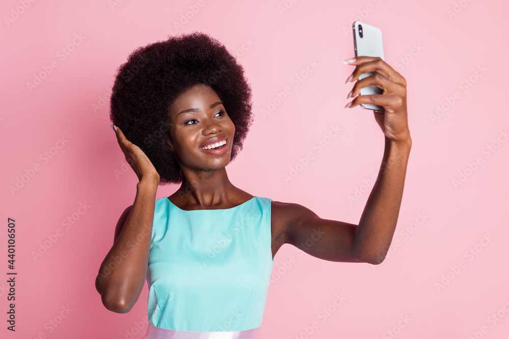 Photo portrait of pretty girl in blue dress smiling taking selfie with smartphone touching hair isolated on pastel pink color background Photo portrait of pretty girl in blue dress smiling taking selfie with smartphone touching hair isolated on pastel pink color background