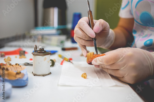 Close-up of a dental technician shaping a prosthesis tooth with a tool at work desk.