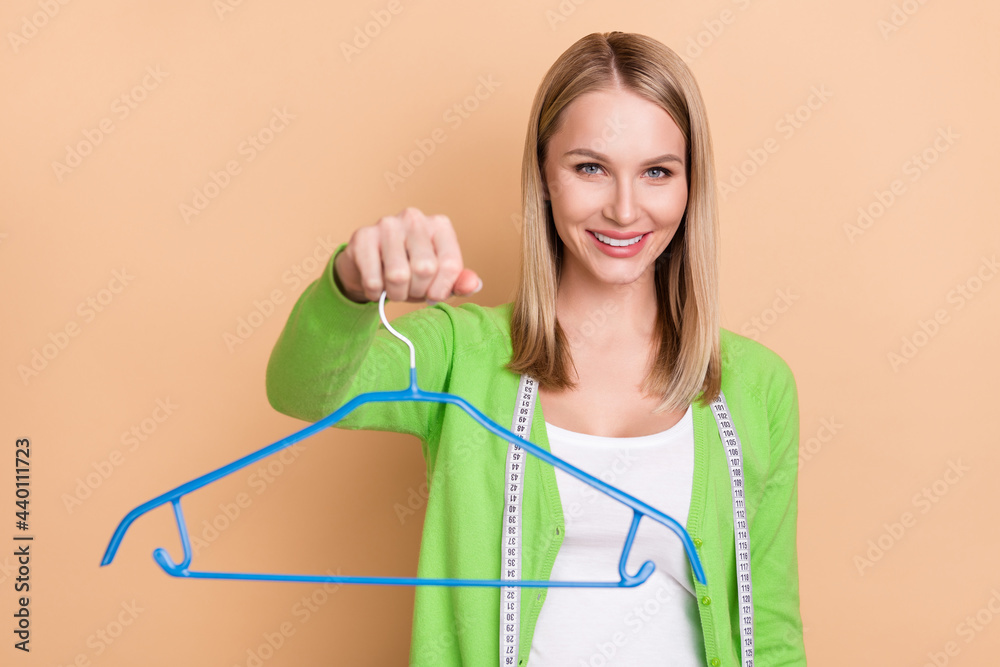 Portrait of attractive cheerful girl designer giving you garmnent hanger isolated over beige pastel color background Portrait of attractive cheerful girl designer giving you garmnent hanger isolated over beige pastel color background