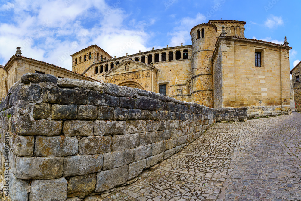 Panoramic of old stone Romanesque church with cobblestone pavement and blue sky. Santillana del Mar.