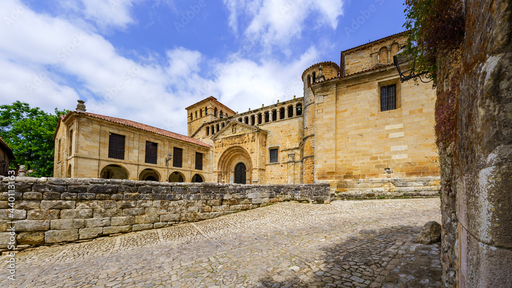 Panoramic of old stone Romanesque church with cobblestone pavement and blue sky. Santillana del Mar.