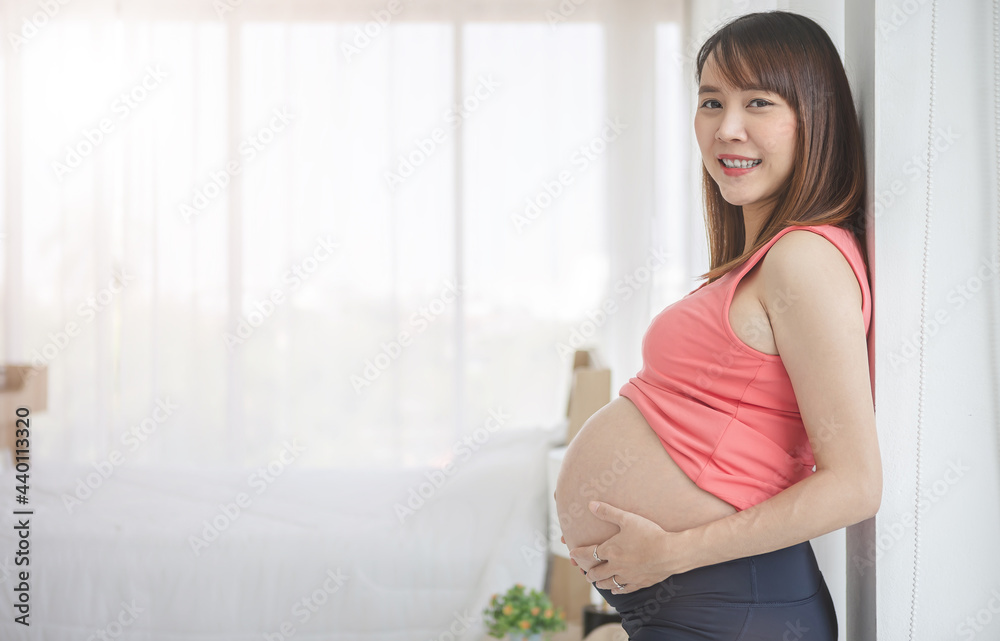 Pregnant woman taking care of her child by holding baby in her pregnant belly in the bedroom