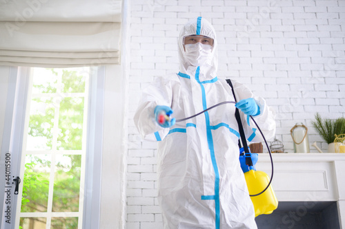 A medical staff in PPE suit is using disinfectant spray in living room, Covid-19 protection , disinfection concept .