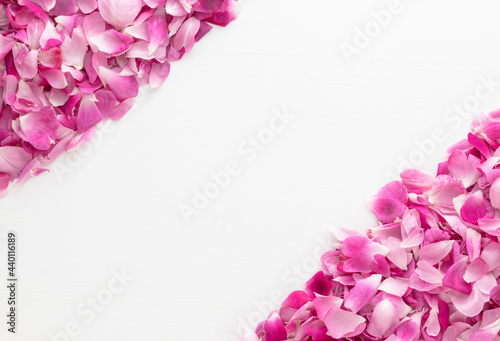 Pink rose petals on left upper and right bottom corner on white wooden background.