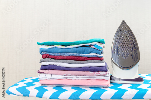 Stack of colorful cotton clothes and iron.Household laundry ironing.