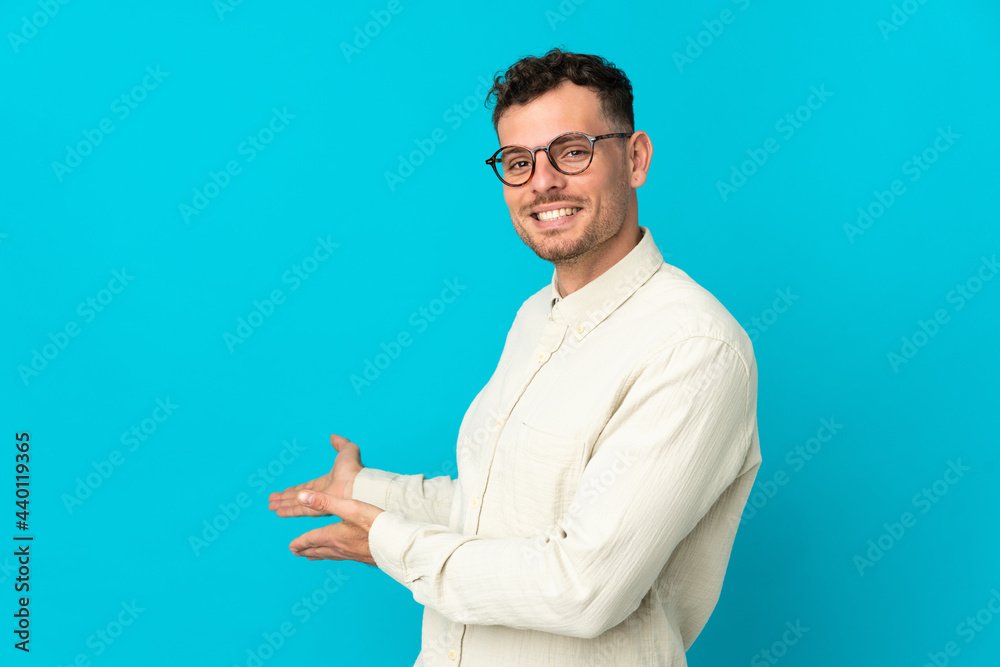 Young caucasian handsome man isolated on blue background extending hands to the side for inviting to come Young caucasian handsome man isolated on blue background extending hands to the side for inviting to come