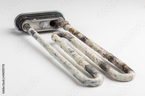 Old broken electric heater of washing machine with limescale and rust on white background. Scum and scale on heating element photo