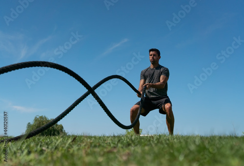 Male athlete on the outdoor in the park, exercises for endurance, using a thick rope, for cross fitness. European
