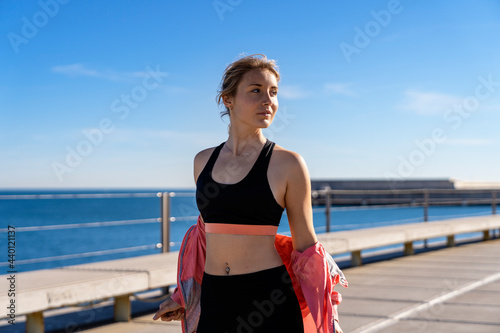 Beautiful female jogger removing jacket while looking away during sunny day photo