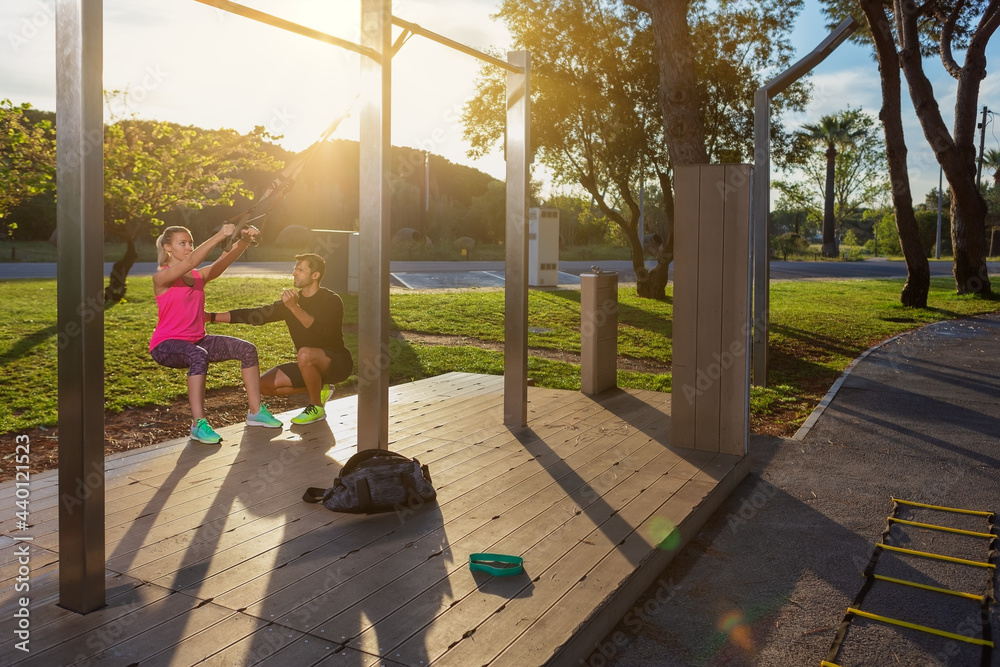 Personal fitness trainer and young woman client, corrects exercises with straps. In park in the morning. Sunny day. Personal fitness trainer and young woman client, corrects exercises with straps. In park in the morning. Sunny day.