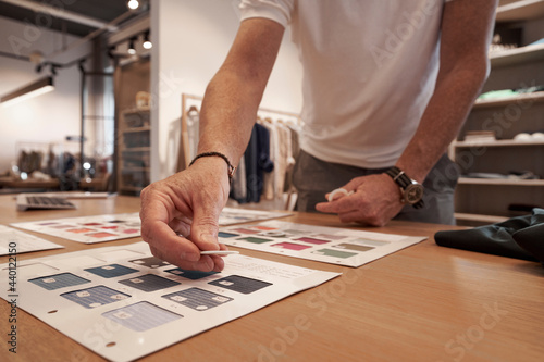 Male designer choosing fabric swatch from catalog at clothes design studio