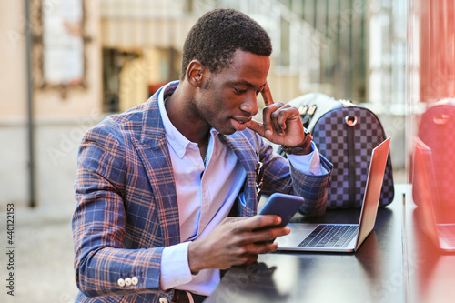 Young male entrepreneur with mobile phone using laptop at sidewalk cafe