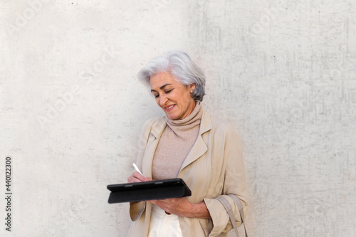 Smiling mature woman with digital tablet and digitized pen in front of wall photo