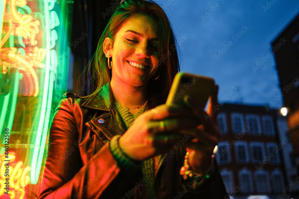 © Angel Santana Garcia/Westend61 - Smiling woman using mobile phone standing by illuminated light © Angel Santana Garcia/Westend61 - Smiling woman using mobile phone standing by illuminated light
