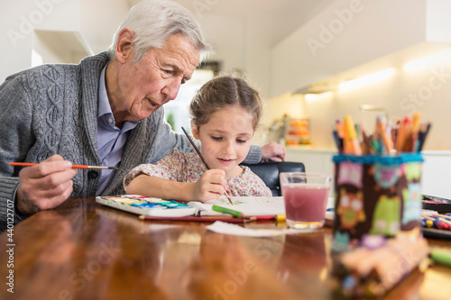Granddaughter and grandfather painting together at home photo