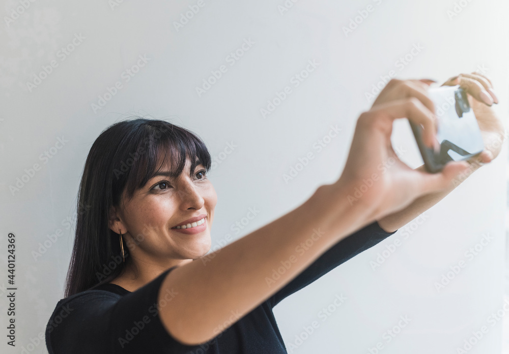 Smiling mid adult woman taking selfie through mobile phone at home Smiling mid adult woman taking selfie through mobile phone at home