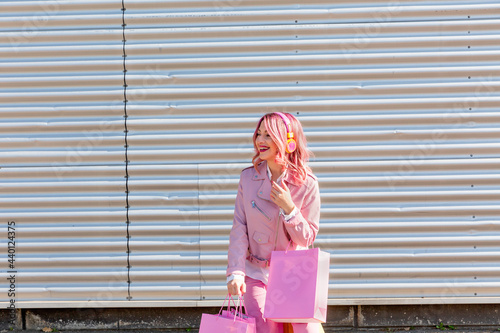 Happy young woman with pink shopping bags standing in front of corrugated wall