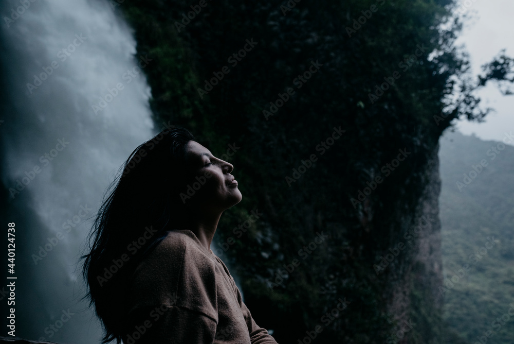 Woman with eyes closed standing at waterfall