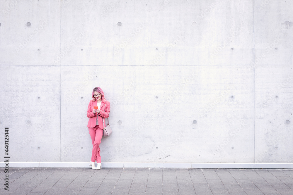 Woman in smart casual using mobile phone in front of concrete wall Woman in smart casual using mobile phone in front of concrete wall