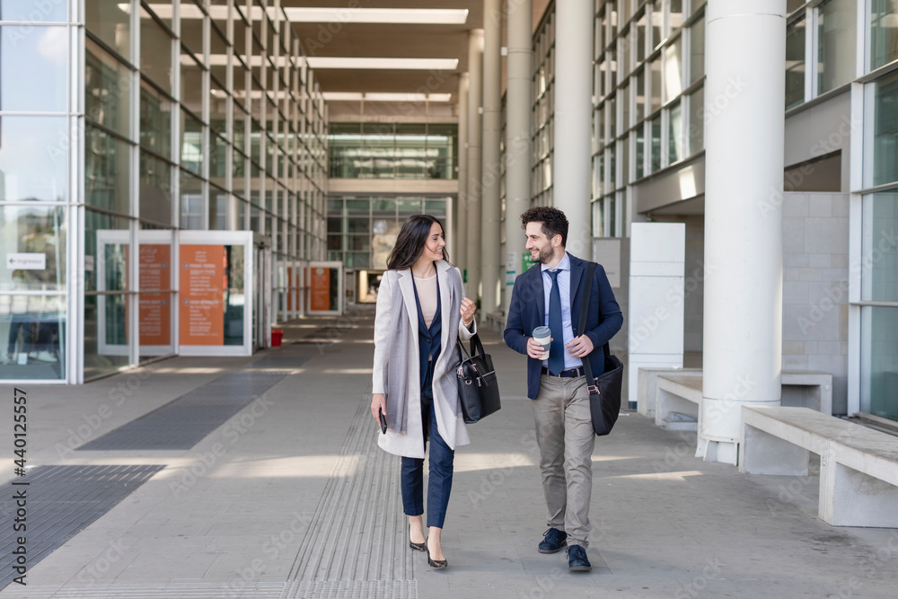 Male and female colleagues talking while walking on footpath Male and female colleagues talking while walking on footpath