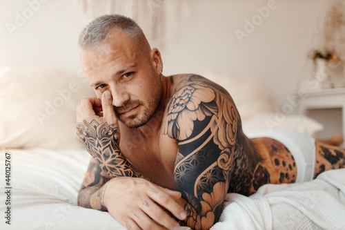 Serious man with tattoo lying on bed at home