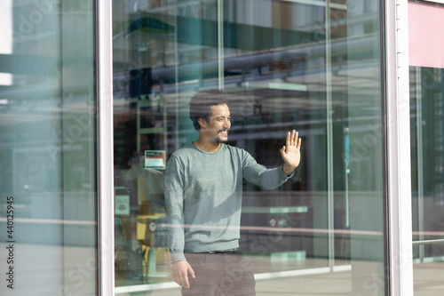 Smiling man looking away while touching glass wall