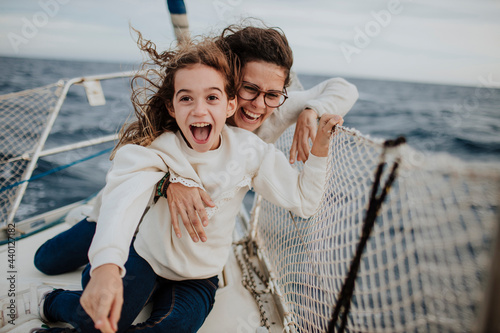 Laughing mother with excited daughter on sailboat during vacation photo