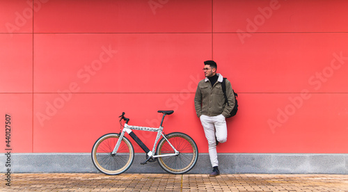 Young businessman by bicycle leaning on red wall